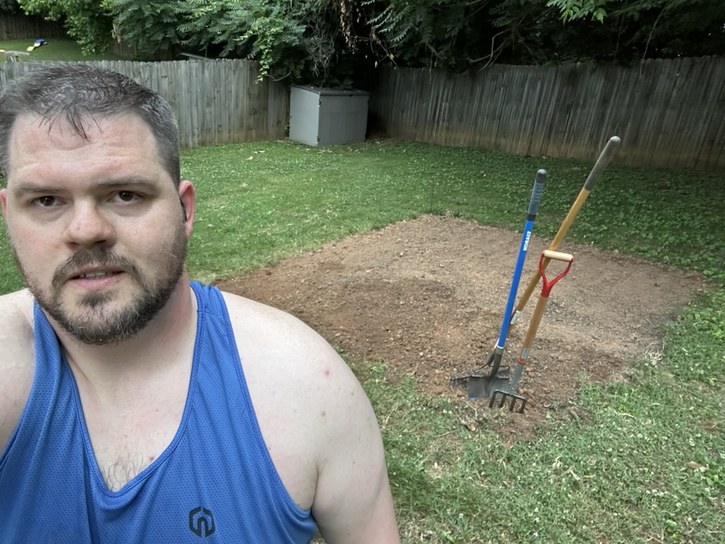 Nathan in the yard with a fork and spade beside the first cleared patch, June 22